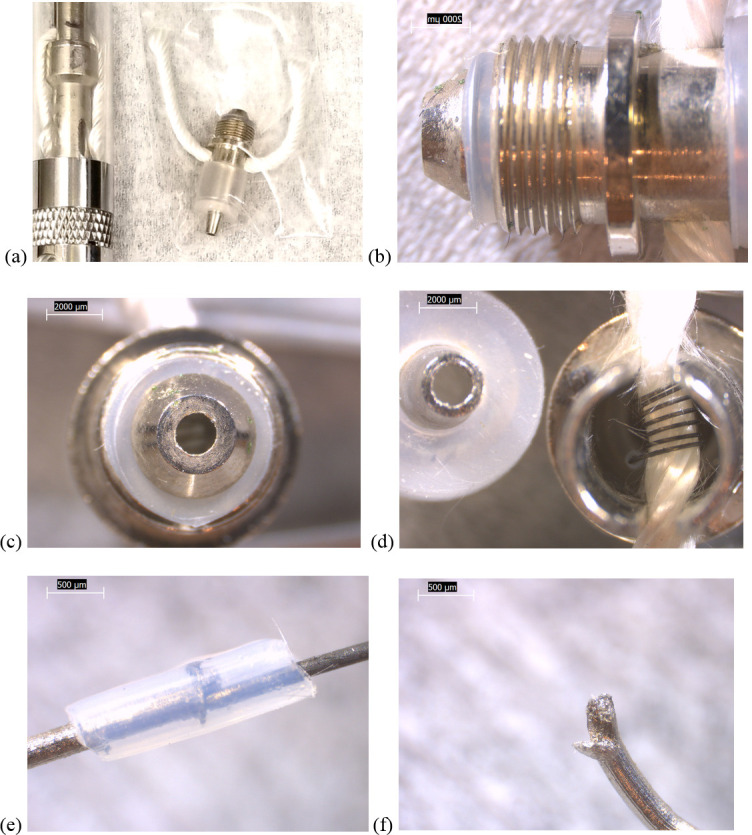 Images of components from new EGO-CE5 coil head.a) camera image showing coil head with wick, next to unit containing empty tank, air tube, and battery contact. b)–f) 6.3-40x stereozoom microscope images: b) side view of threaded battery contact end. c) top view of (b). d) opposite view of coil head with air tube nozzle removed and slotted wick-filament holder visible. e) Clear polymer sheath wrapped around one filament-wire joint. f) End of wire lead that touches battery contact.